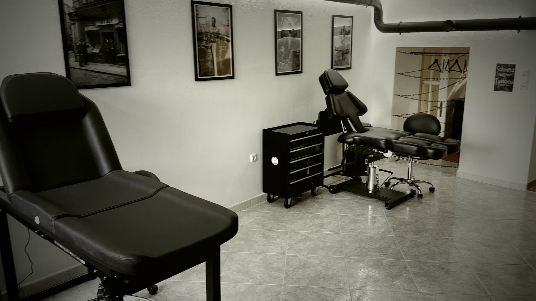 Schwarzer Tattoo-Liegestuhl in einem dunkel eingerichteten Atelier mit Lampe, Pflanzen und gerahmten Bildern